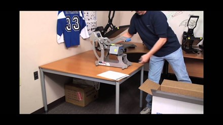 Man in office with a Hotronix Auto Cap Heat Press on desk with a hockey jersey hanging on the wall
