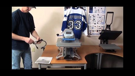 Man in office with a Hotronix Fusion IQ Heat Press on desk with a hockey jersey hanging on the wall